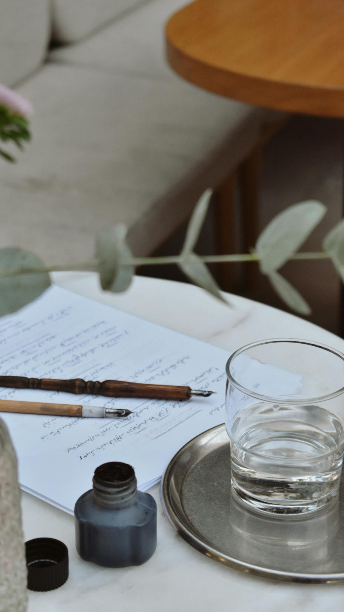 A tranquil still life scene featuring writing tools, ink, and a glass on a textured table.