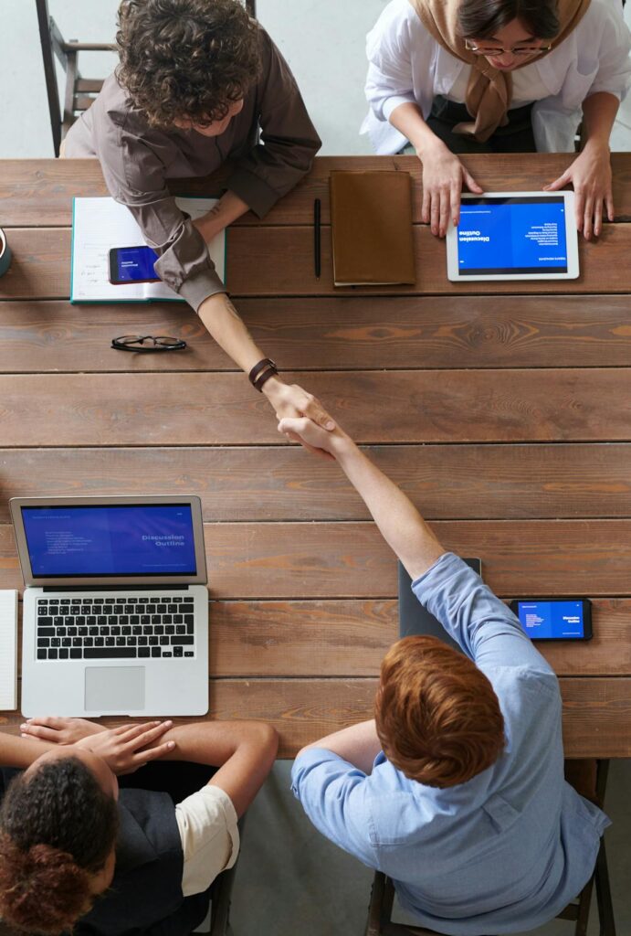 Overhead view of colleagues in a work meeting using laptops and tablets, emphasizing teamwork and technology.